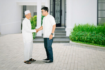 Elderly man handshaking with son in front of house