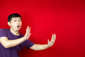 An asian man with a funny face trying to signal stop with both hands to stop.