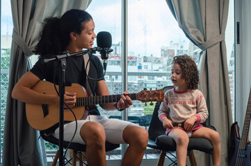 young father sings with the guitar to his daughter sitting in his home music studio