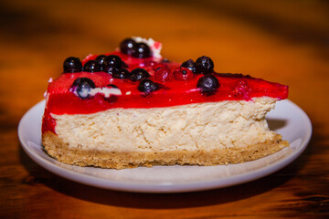 Slice of cheese cake with black currant berries on a table in a white plate.
