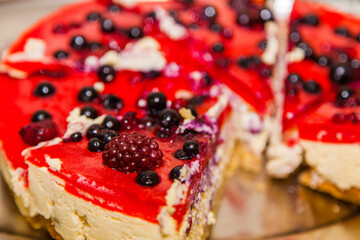 Slice of cheese cake with black currant berries on a table in a white plate.