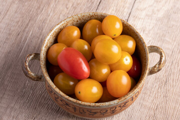 small yellow tomatoes in a cup on wooden background