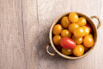 small yellow tomatoes in a cup on wooden background
