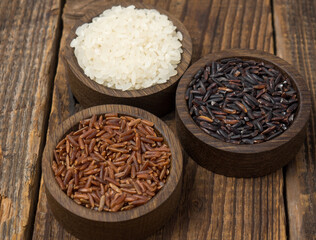 Three types of rice in wooden bowls on an old wooden table. red ,black and white rice ,copy space