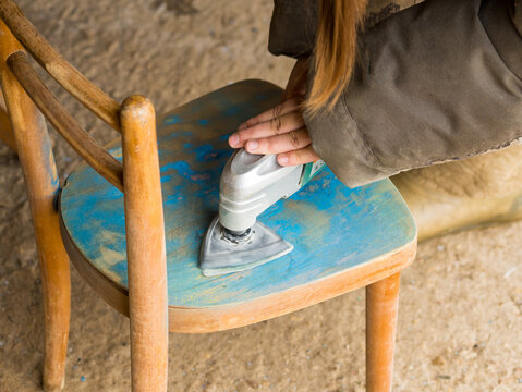 A Girl Using A Grinder Removes Old Paint From Furniture, Restoration Of Antique Furniture