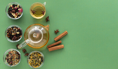 several types of herbal tea mixtures in a glass dish next to a kettle and a cup of hot tea on a...