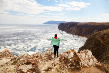 A woman admires the boundless expanses of Lake Baikal. Travel in the spring. White ice floes melt...