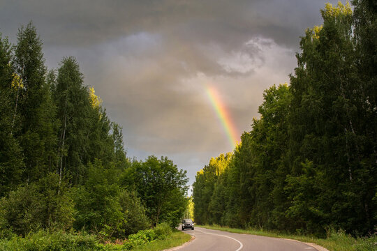 Rainbow over the asphalt road through the forest