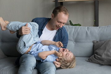 Smiling bonding 35s young father tickling laughing cute little kid son, having fun together on weekend at home, enjoying carefree playtime activity at home, sincere loving family relations concept.