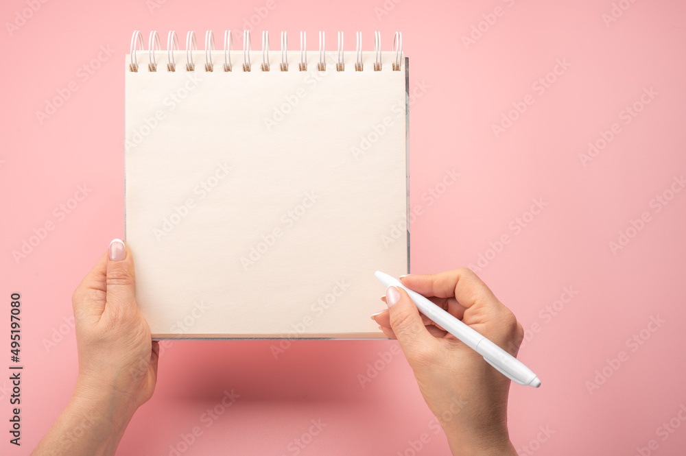 Aufkleber mockup notepad. writing in blank notepad on pink background. woman hand with pen next to an empty bl