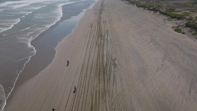 Aerial: dirt bikers travelling along Muriwai beach, New Zealand