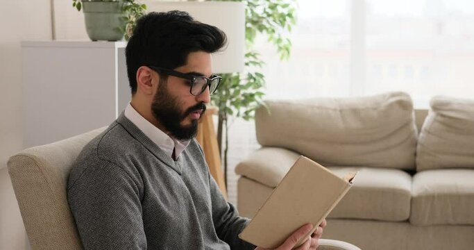 Thoughtful man reading a book sitting on armchair at home