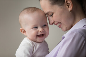 Head shot close up sincere loving millennial mother touching forehead with laughing adorable joyful baby boy girl, expressing candid feelings, enjoying happy motherhood, family devotion concept.