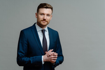 Serious male entrepreneur keeps hands together wears formal clothes dressed in office attire poses against grey background with copy space