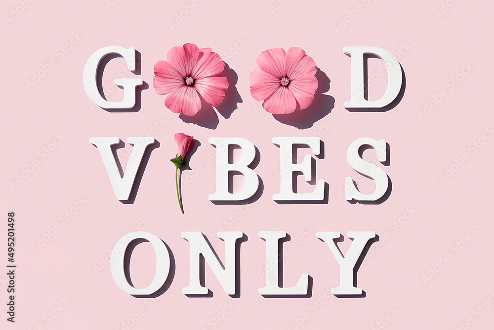 Wall mural good vibes only. motivational quote from white letters and beauty natural flowers on pink background