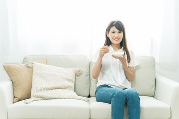Obraz premium ソファでヨーグルトを食べる女性（笑顔） 