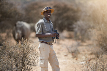 Never a dull moment on the job. Portrait of a confident game ranger looking at a group of rhinos in...