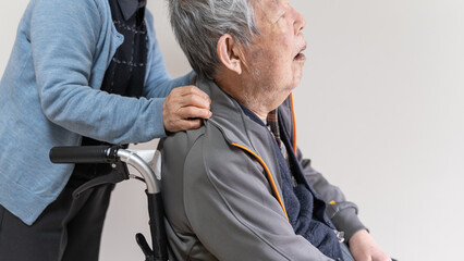 車椅子に乗った高齢者の旦那の肩に手を置く老人妻