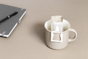 Drip coffee bag with ground coffee in big cup on office table, package with paper bag drip coffee...