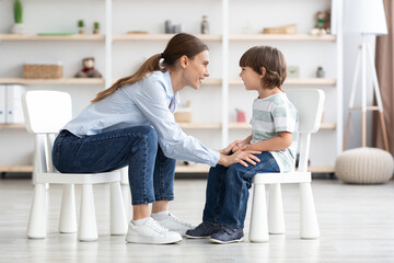 Professional young woman therapist communicating with happy little boy, talking during personal...