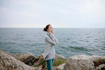 pretty woman in a gray sweater stands on a rocky shore nature female relaxing