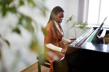 African young woman sitting behind the grand piano and learning to play the classical music in the class