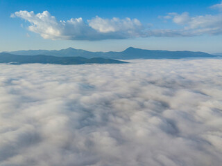 Flight over fog in Ukrainian Carpathians in summer. Mountains on the horizon. A thick layer of fog covers the mountains with a continuous carpet. Aerial drone view.