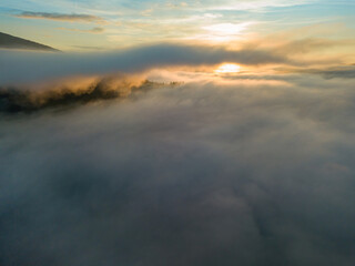 The rays of dawn over the fog in the Ukrainian Carpathians. Aerial drone view.