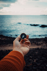 Pov of man hand holding navigational travel compass to find direction and next destination place. Concept of travel people and exploring. Beach and ocean with sky light in background © simona