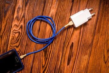 Mobile phone and charger on brown wooden background
