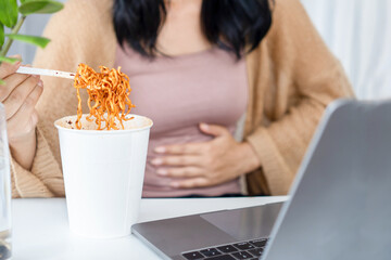businesswoman eating spicy noodle and having stomachache at office desk