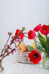 easter colorful eggs with tulips and spring flowers on a white wooden background