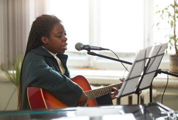 African student sitting in front of the sheet music and singing a song to microphone while playing...