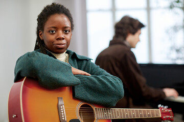 Portrait of African young woman sitting with guitar and looking at camera, she studying at musical...