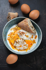 Bowl with cilbir or a turkish dish of poached eggs and yogurt, vertical shot on a dark-brown stone background, elevated view