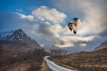 Digital composite image of hot air balloons flying over Stunning Winter sunset landscape of Etive Mor road leading between the mountains of the Scottish Highlands