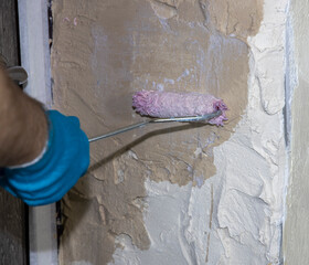 A man in blue gloves applies a primer with a roller. Repair and priming of the wall before applying...
