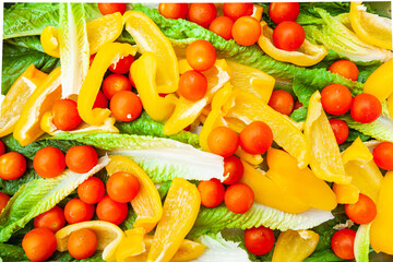 Fresh salad of whole cherry tomatoes, sliced yellow bell peppers and lettuce leaves.