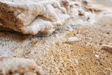 Fototapeta na wymiar Sand and stones covered with crystalline salt crust on shore of Dead Sea, closeup detail