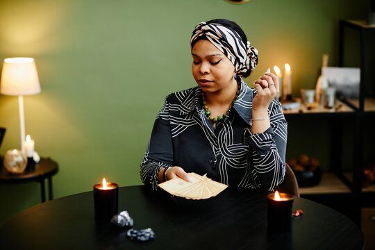 Portrait of young black woman reading tarot cards in fortune tellers shop lit by candles, copy space