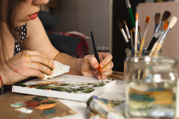 Selective focus close-up portrait of a woman artist who paints with oil paints on canvas with a...