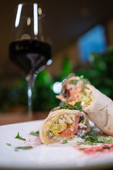 pita roll with chicken, tomato and cheese on white plate with sauce and red wine