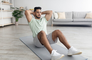Handsome young Arab man exercising on yoga mat, strengthening abs muscles at home, copy space