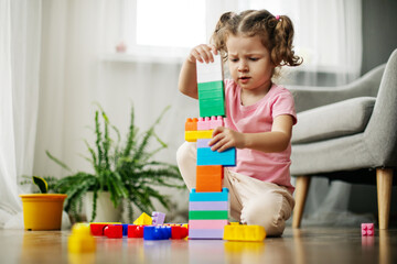 A little girl is sitting on the floor in the playroom and playing with colorful cubes, a constructor.