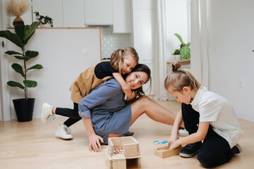 Friendly family playing on the floor. Mom and two children. Building house from wooden blocks. Low angle.