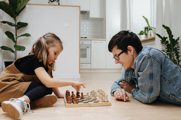 Match of chess between dad and his child daughter. Both excited and having fun. Side view. On the...
