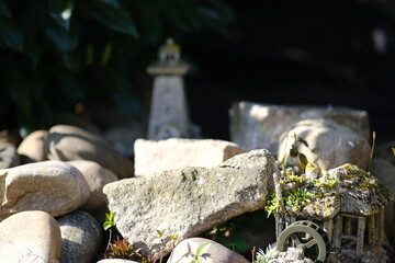 Natursteine und Gewächse im Sonnenlicht im WInter in einem Garten. Im Hintergrund steht eine Leuchtturm Miniatur