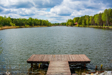 Background with wooden pier on the shore of a large lake in the forest. Wonderful spring landscape. A cozy place for rest, meditation and fishing
