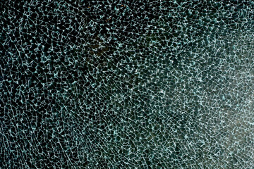 Broken automotive glass with small cracks on a dark background.