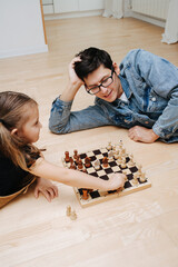 Cheeky child girl playing chess with her dad. Both excited and having fun. Side view. On the...